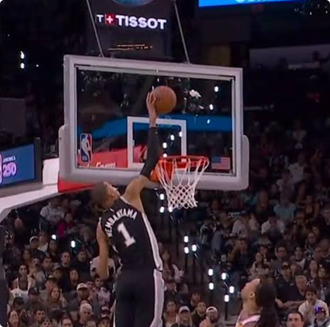 Basketball player in a black jersey (no. 1) jumping for a slam dunk at the basket as the crowd watches, with arena signage visible above the backboard.